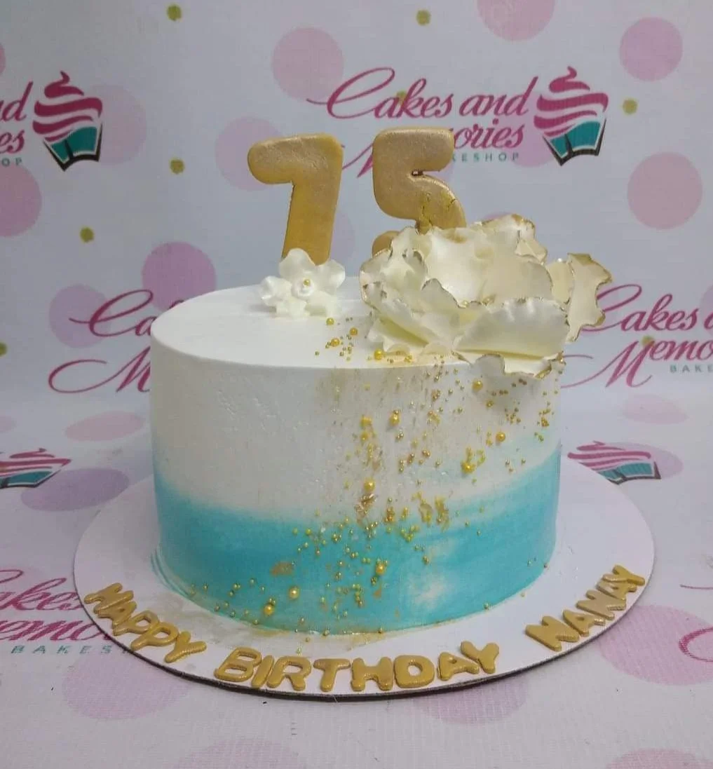 Senior Birthday White Floral Cake A white and light blue gradient 1 Tier cake, featuring a gold number 75, white edible flowers, gold sprinkles, and gold text.
