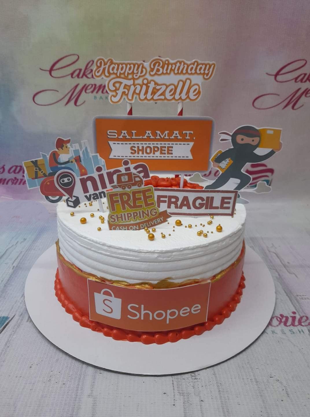 Shopee and Ninja Van themed birthday cake with orange and white icing, delivery character toppers, and gold dragees. Shopee and Ninja Van themed birthday cake with orange and white icing, delivery character toppers, and gold dragees.