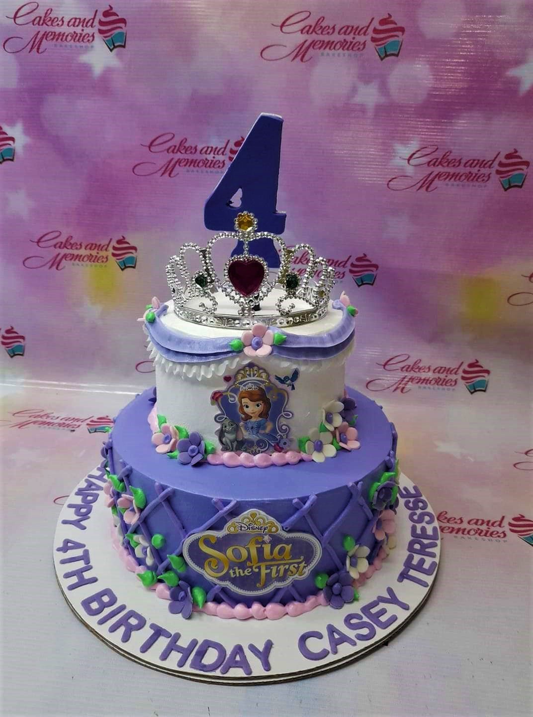 Two-tier Sofia the First themed birthday cake in purple and white with a silver tiara and floral decorations. Two-tier Sofia the First themed birthday cake in purple and white with a silver tiara and floral decorations.