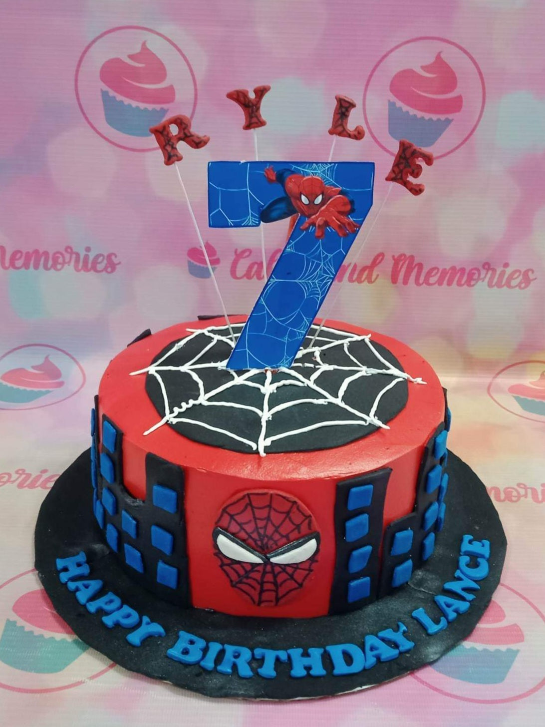 Red Spiderman birthday cake with black city skyline, spider web top, and a large number 7 topper featuring Spiderman. Red Spiderman birthday cake with black city skyline, spider web top, and a large number 7 topper featuring Spiderman.