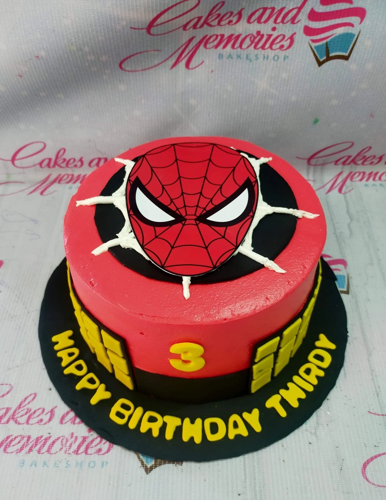 Red Spiderman birthday cake with a large Spiderman face printout, white icing webs, and yellow fondant number 3.