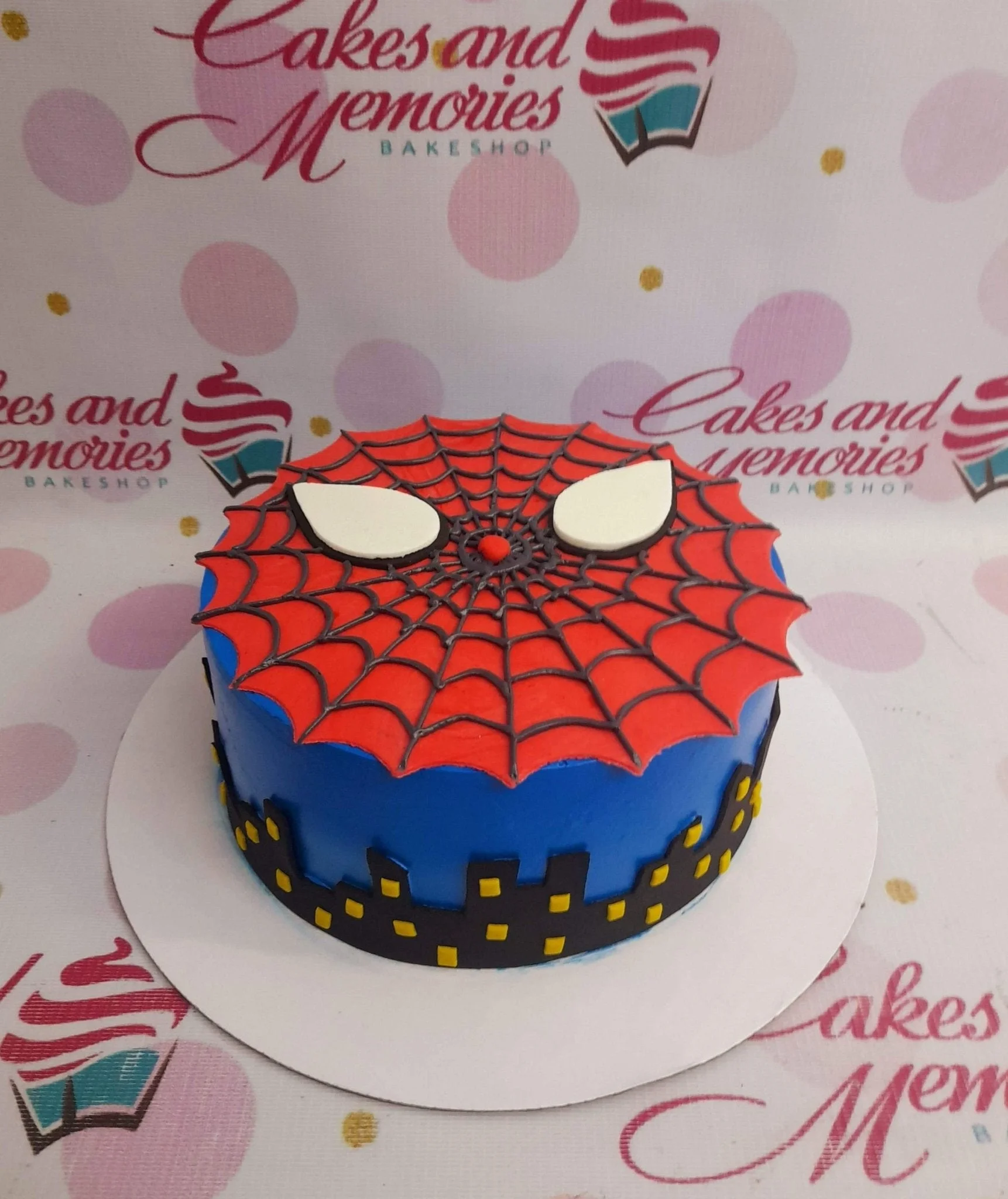 Blue Spiderman themed birthday cake with a red spiderweb top and black city skyline silhouette on the sides.