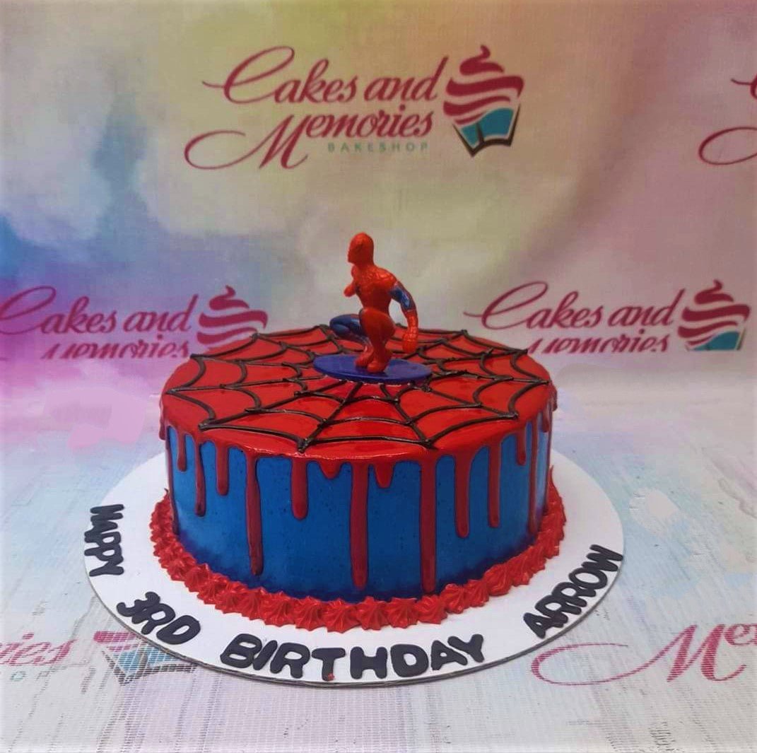Spiderman themed birthday cake with blue icing, red drip, and a black spiderweb design on top featuring a Spiderman figurine. Spiderman themed birthday cake with blue icing, red drip, and a black spiderweb design on top featuring a Spiderman figurine.