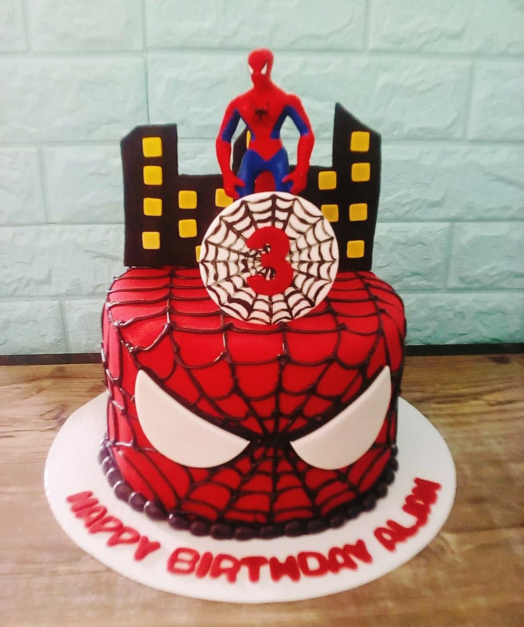 Spiderman themed red fondant cake with black web design, white eyes, and a Spiderman figurine on top with a city skyline backdrop. Spiderman themed red fondant cake with black web design, white eyes, and a Spiderman figurine on top with a city skyline backdrop.