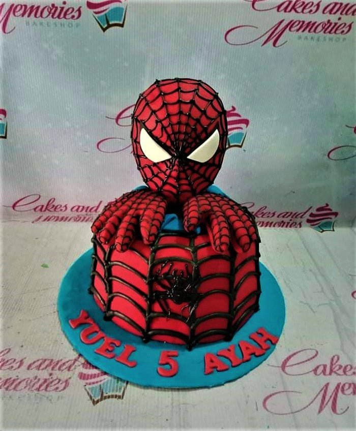 Spiderman themed birthday cake with a 3D fondant Spiderman head and hands on a red webbed cake with a blue base. Spiderman themed birthday cake with a 3D fondant Spiderman head and hands on a red webbed cake with a blue base.