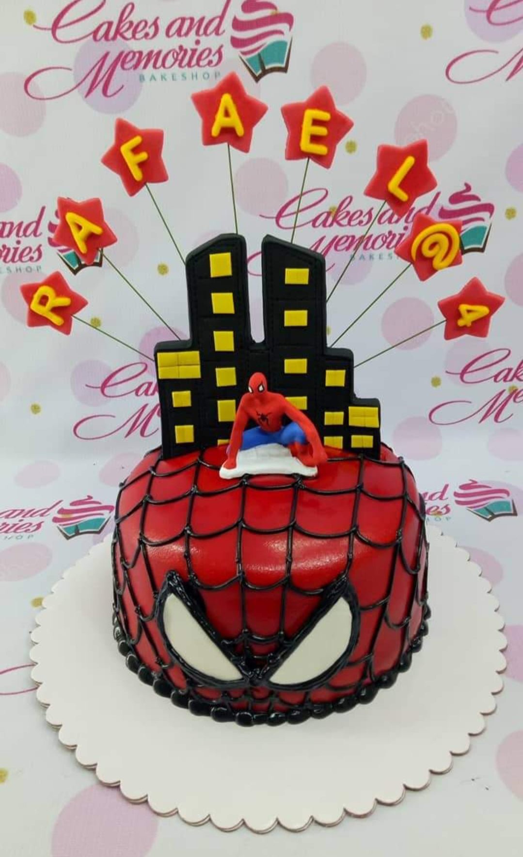 Red Spiderman themed birthday cake with black webbing, large white eyes, and a 3D Spiderman figure on top with city buildings. Red Spiderman themed birthday cake with black webbing, large white eyes, and a 3D Spiderman figure on top with city buildings.