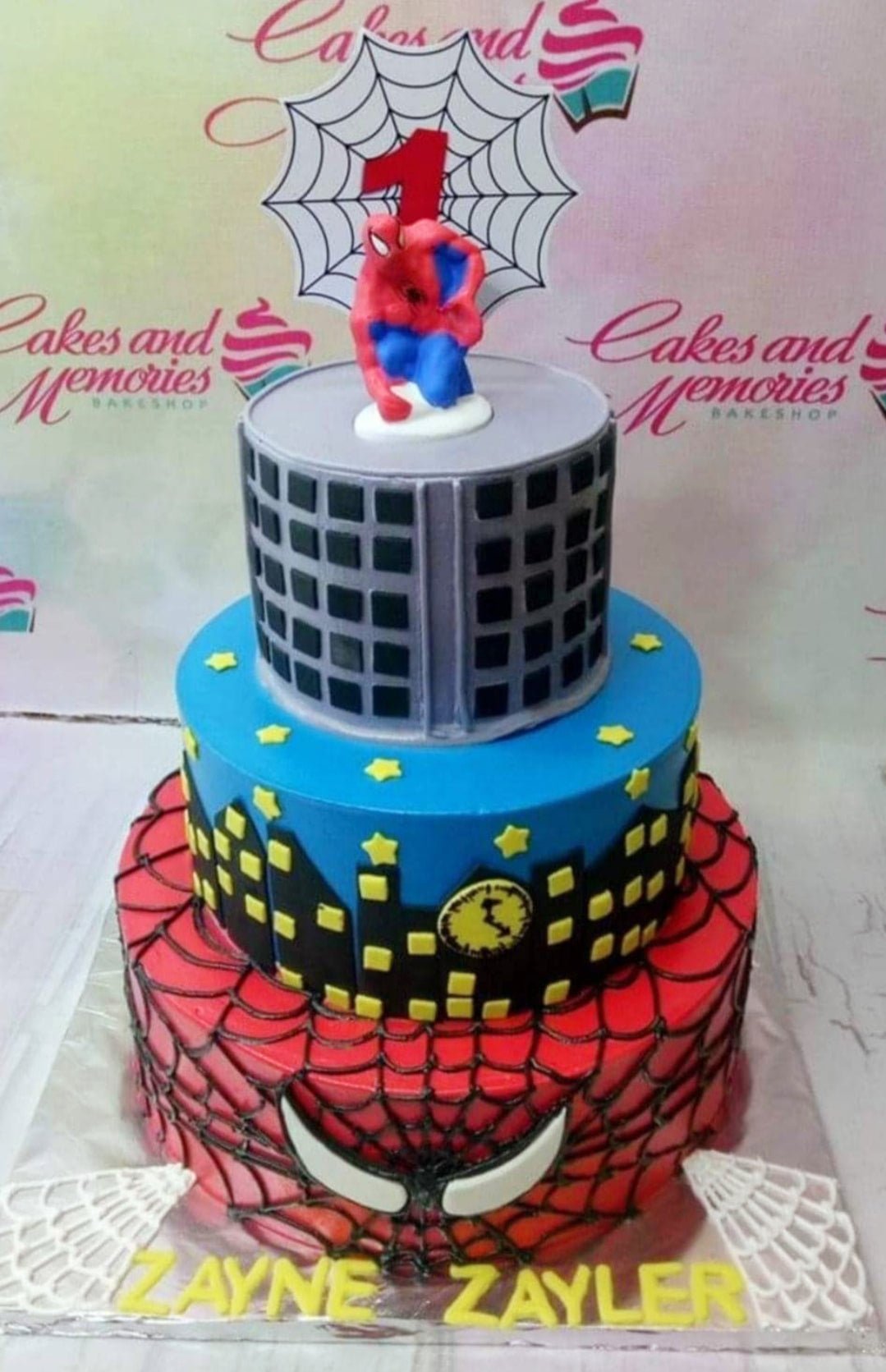3-tier Spiderman themed birthday cake with city skyline, spider web patterns, and a Spiderman figure on top. 3-tier Spiderman themed birthday cake with city skyline, spider web patterns, and a Spiderman figure on top.