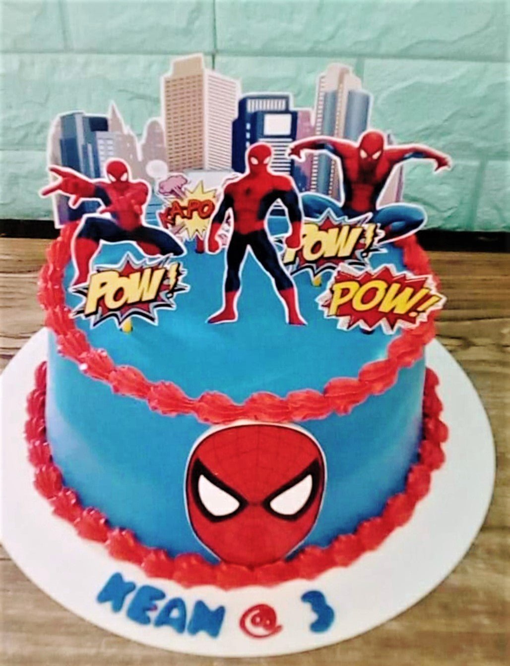 Blue Spiderman birthday cake with red icing borders and printed superhero toppers Blue Spiderman birthday cake with red icing borders and printed superhero toppers