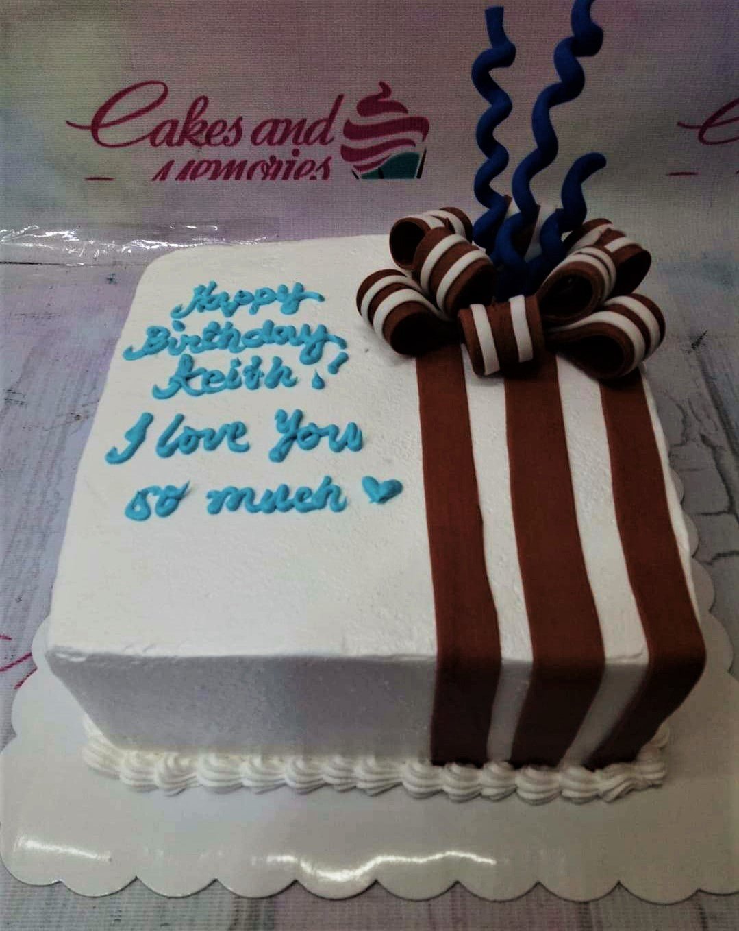 Square white soft-icing cake with brown vertical stripes, a large brown and white fondant bow, and blue curly toppers. Square white soft-icing cake with brown vertical stripes, a large brown and white fondant bow, and blue curly toppers.