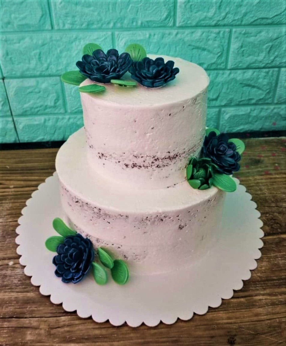 Two-tier semi-naked chocolate cake decorated with dark blue and green gumpaste succulent flowers on a white scalloped base. Two-tier semi-naked chocolate cake decorated with dark blue and green gumpaste succulent flowers on a white scalloped base.