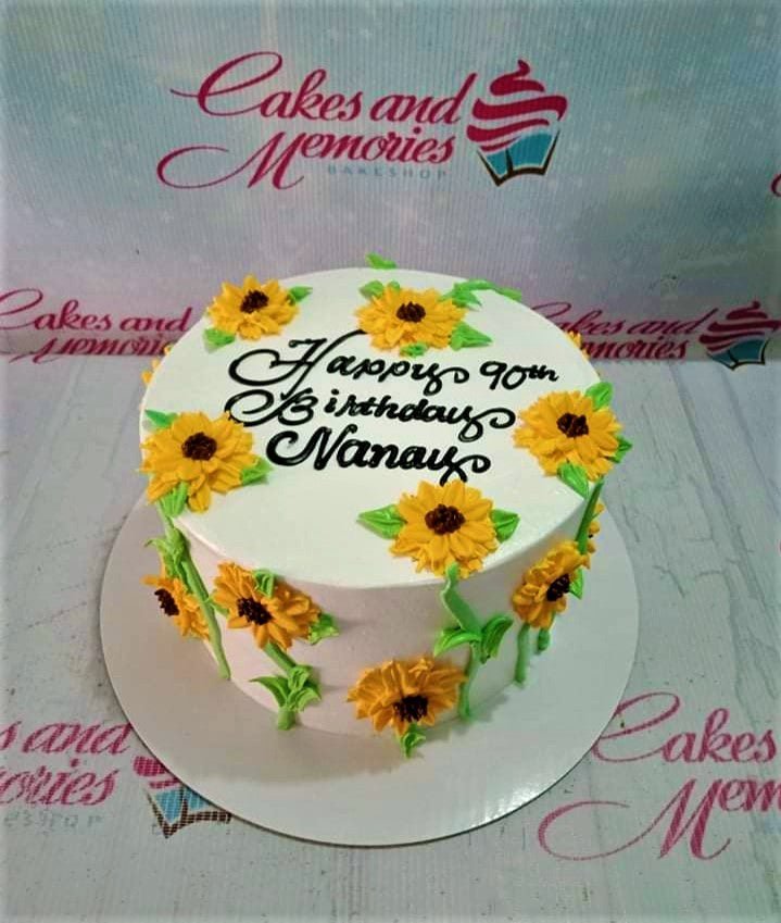 White 1-tier birthday cake decorated with yellow piped icing sunflowers and green leaves with a black icing message for Nanay's 90th birthday. White 1-tier birthday cake decorated with yellow piped icing sunflowers and green leaves with a black icing message for Nanay's 90th birthday.