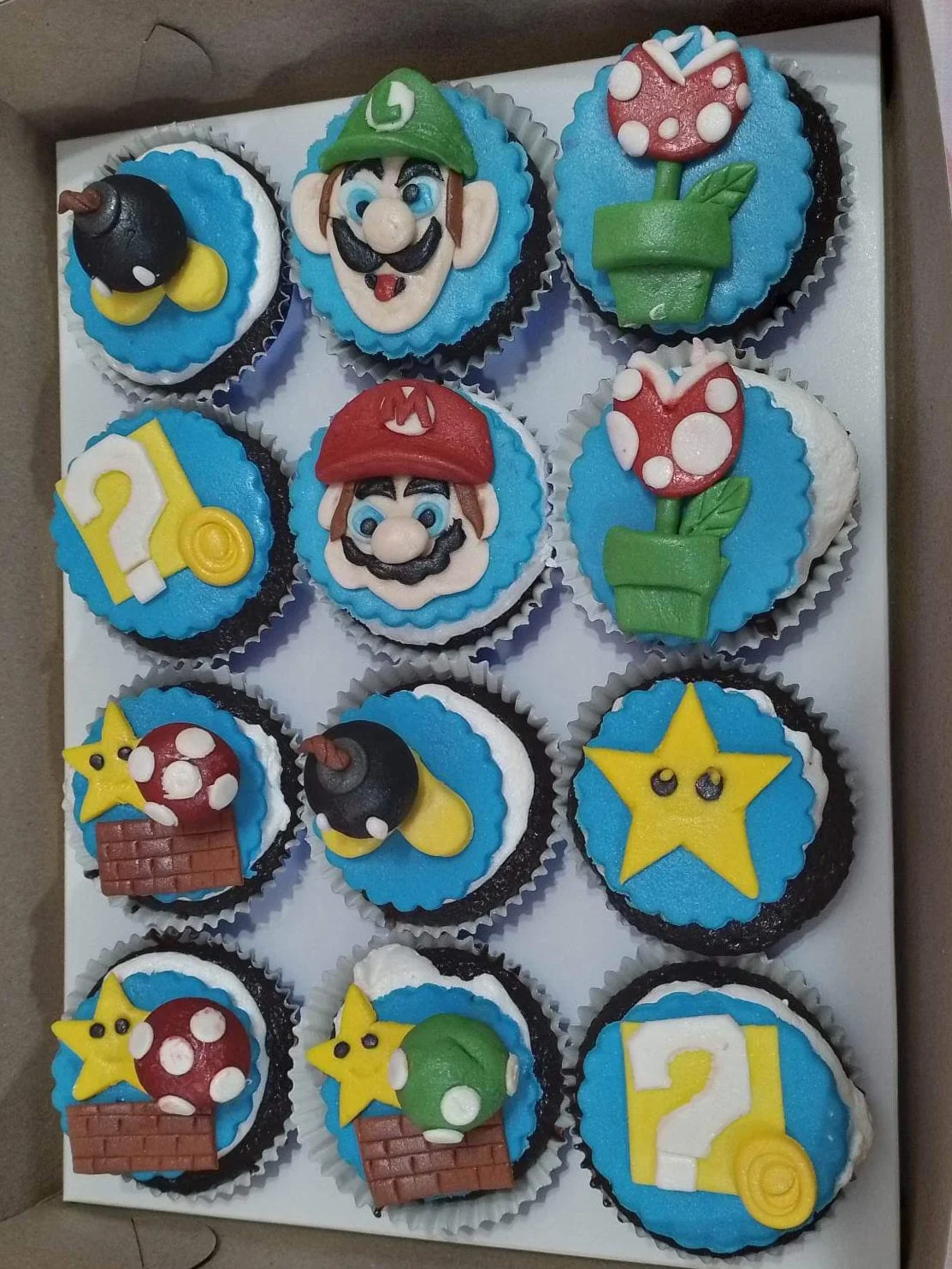 Super Mario themed cupcakes with fondant toppers of Mario, Luigi, Piranha Plants, Bob-ombs, and Question Blocks on blue icing. Super Mario themed cupcakes with fondant toppers of Mario, Luigi, Piranha Plants, Bob-ombs, and Question Blocks on blue icing.