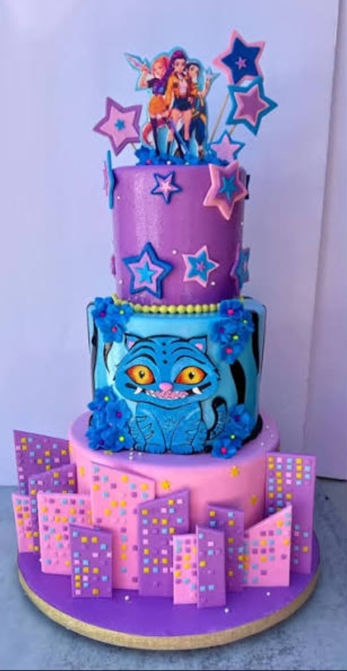 A multicolor 3 tier cake featuring purple and pink city building panels, blue cat character, animated female character printouts, and purple and blue fondant stars. A multicolor 3 tier cake featuring purple and pink city building panels, blue cat character, animated female character printouts, and purple and blue fondant stars.