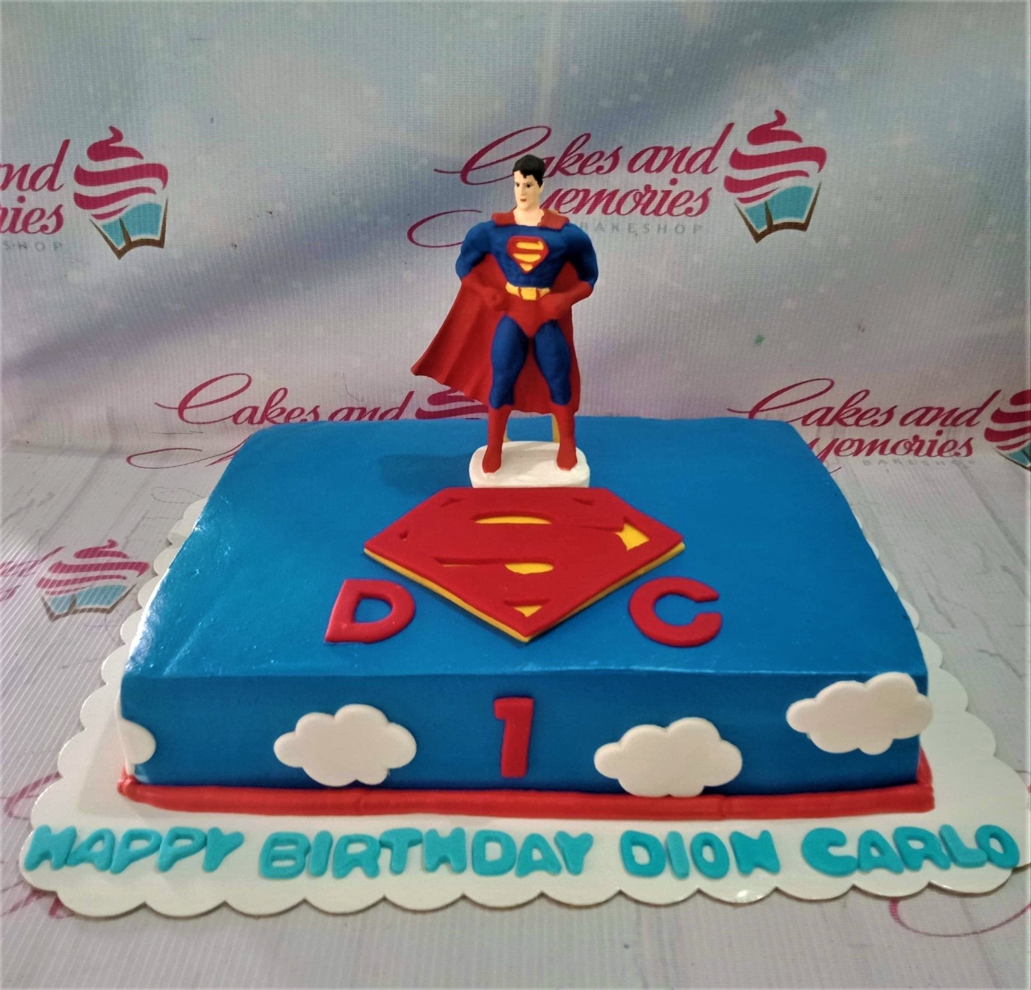 Blue rectangle Superman birthday cake with a 3D Superman figure, red logo, and white clouds. Blue rectangle Superman birthday cake with a 3D Superman figure, red logo, and white clouds.