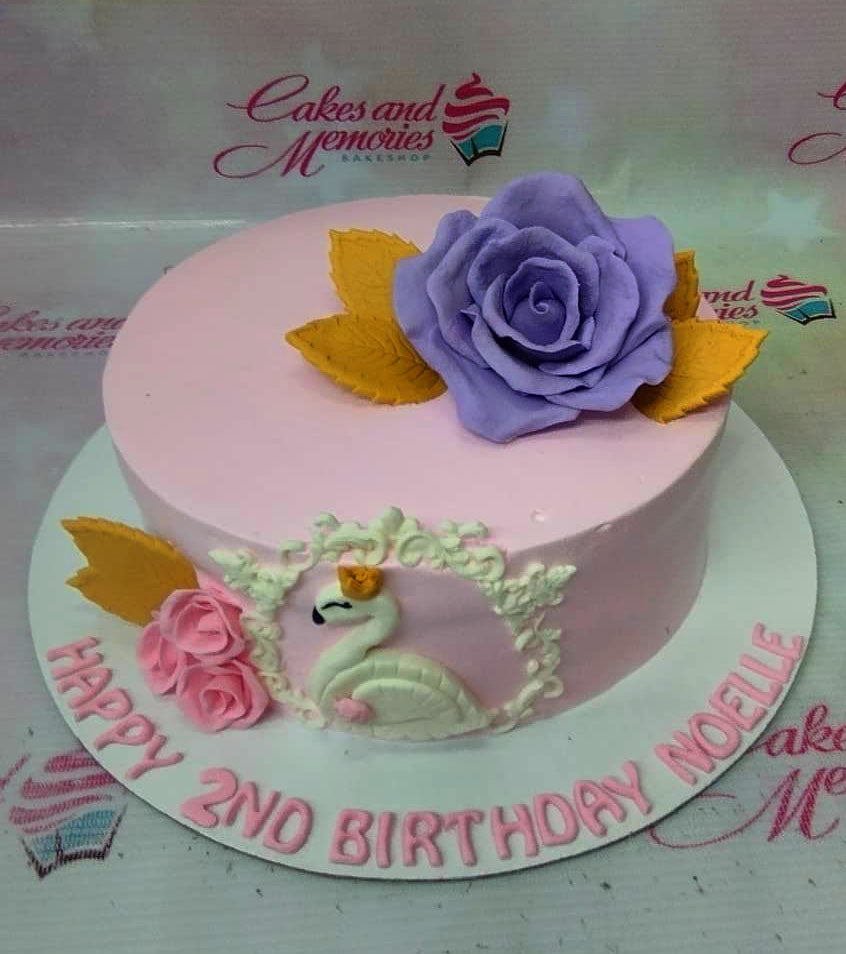 Pink swan birthday cake with a large purple gumpaste rose and gold leaves on a white base board. Pink swan birthday cake with a large purple gumpaste rose and gold leaves on a white base board.