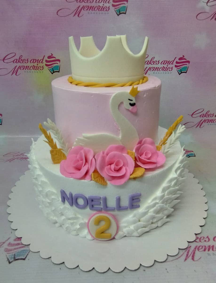 Two-tier swan themed birthday cake in pink and white with a large gold crown topper and pink fondant roses. Two-tier swan themed birthday cake in pink and white with a large gold crown topper and pink fondant roses.