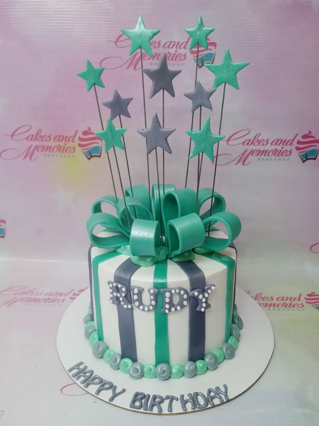 Teal and gray striped fondant birthday cake with a large teal bow and star toppers on wires. Teal and gray striped fondant birthday cake with a large teal bow and star toppers on wires.