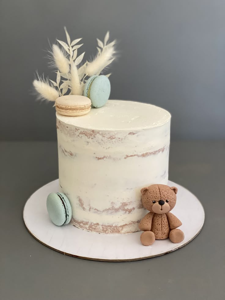 Tall semi-naked cake with a brown fondant teddy bear, blue and beige macarons, and dried floral accents. Tall semi-naked cake with a brown fondant teddy bear, blue and beige macarons, and dried floral accents.