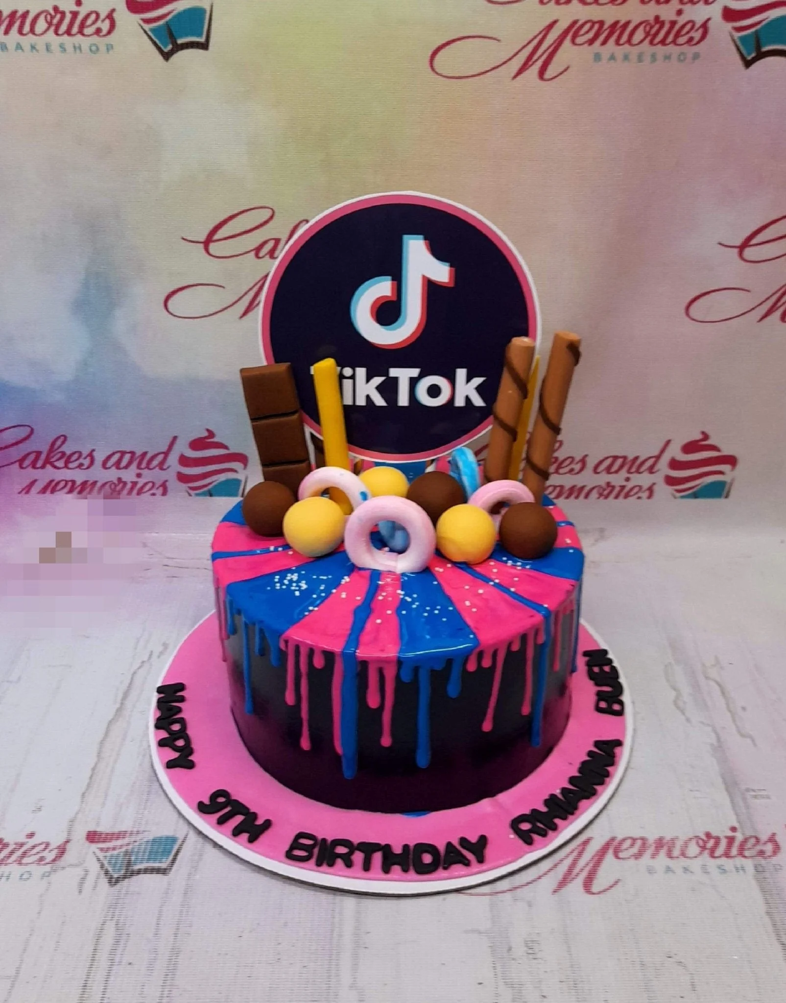 TikTok themed birthday cake with pink and blue drip icing, chocolate bars, and a large TikTok logo topper. TikTok themed birthday cake with pink and blue drip icing, chocolate bars, and a large TikTok logo topper.