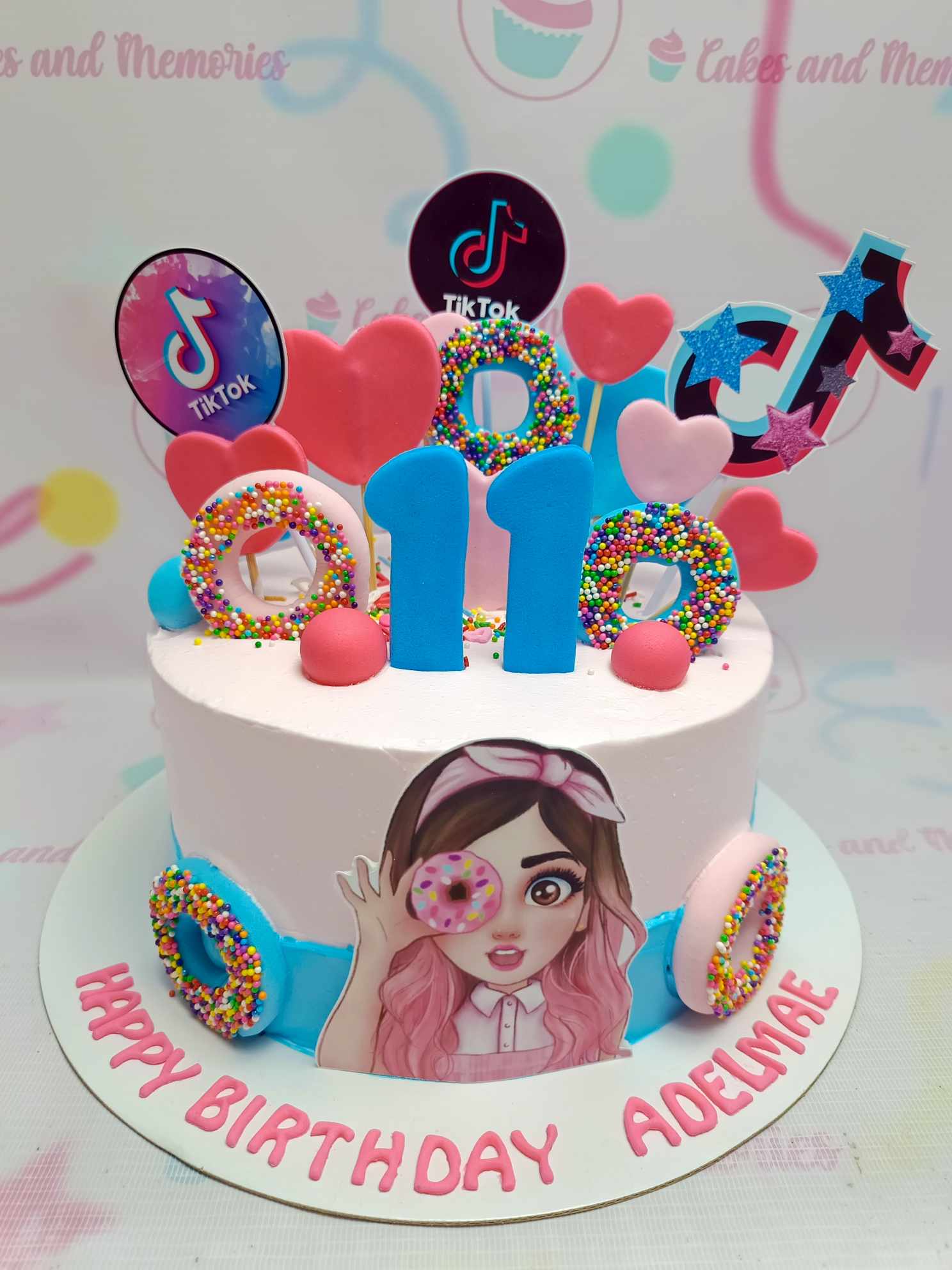 Pink TikTok themed birthday cake with colorful donuts, hearts, and a girl character printout for Adelmae's 11th birthday. Pink TikTok themed birthday cake with colorful donuts, hearts, and a girl character printout for Adelmae's 11th birthday.