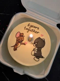 A minimalist white bento cake featuring hand-drawn Tom and Jerry characters with a 6 years together message and a single lit candle. A minimalist white bento cake featuring hand-drawn Tom and Jerry characters with a 6 years together message and a single lit candle.