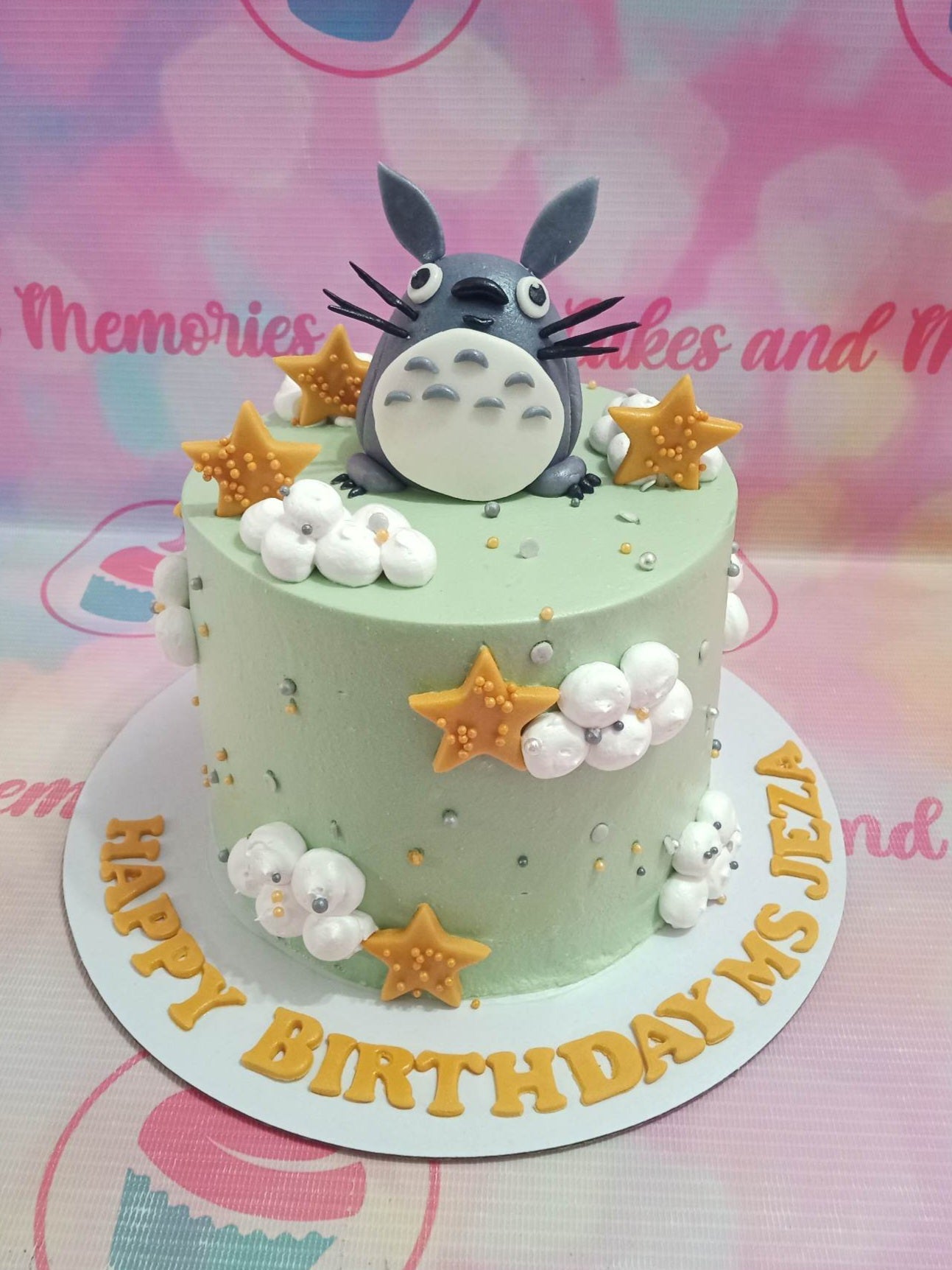 Light green Totoro themed birthday cake with a large fondant Totoro figure, white icing clouds, and gold stars. Light green Totoro themed birthday cake with a large fondant Totoro figure, white icing clouds, and gold stars.