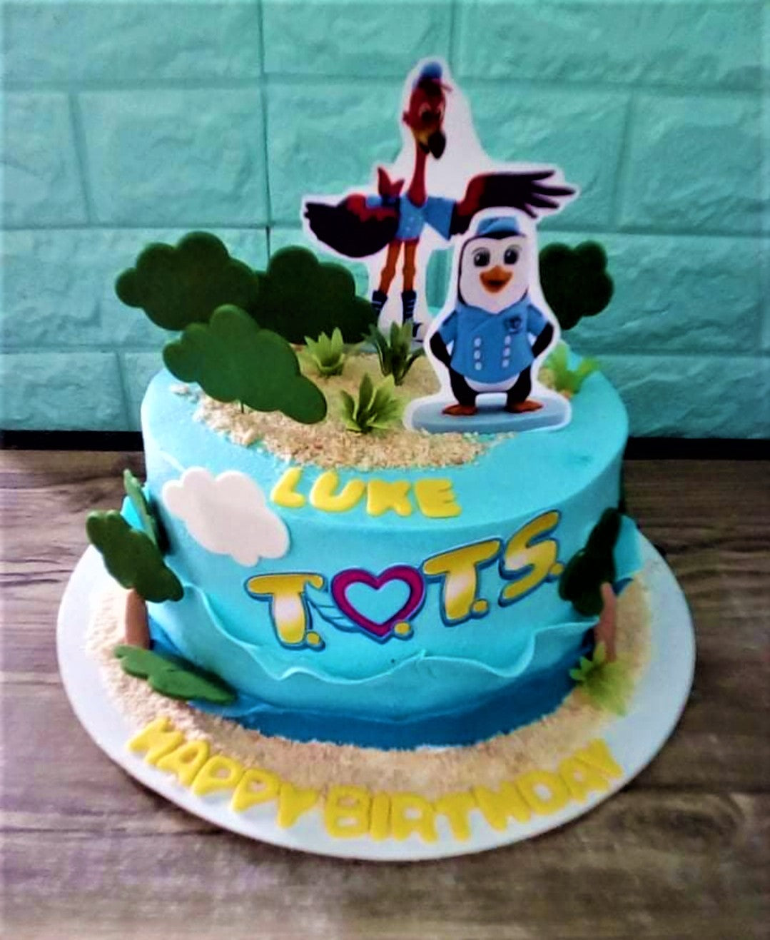 Blue T.O.T.S. themed birthday cake with character printouts, green gumpaste bushes, and sand-like sprinkles. Blue T.O.T.S. themed birthday cake with character printouts, green gumpaste bushes, and sand-like sprinkles.