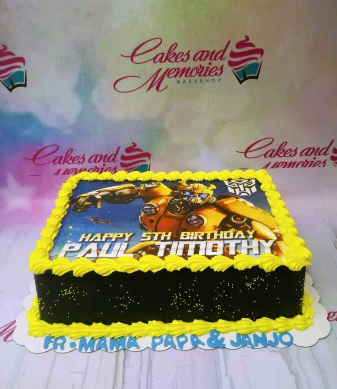 Black rectangular Transformers Bumblebee cake with yellow icing borders and a large printed character topper. Black rectangular Transformers Bumblebee cake with yellow icing borders and a large printed character topper.