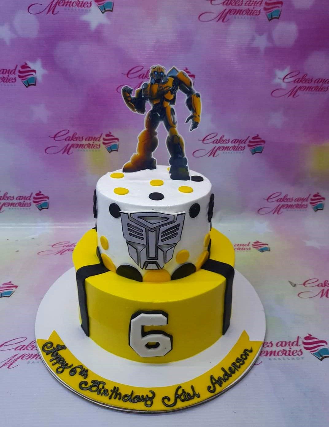 Two-tier Transformers Bumblebee themed birthday cake in yellow and white with black accents and a Bumblebee character topper. Two-tier Transformers Bumblebee themed birthday cake in yellow and white with black accents and a Bumblebee character topper.