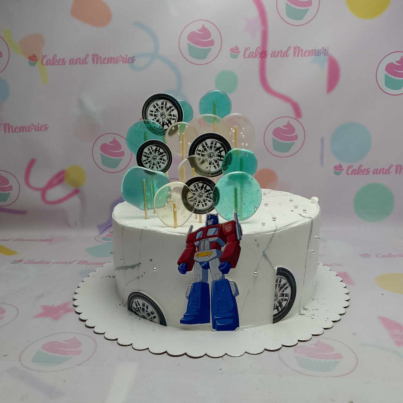 White marble icing cake with Transformers Optimus Prime printout and blue and clear isomalt lollipops and tire decorations. White marble icing cake with Transformers Optimus Prime printout and blue and clear isomalt lollipops and tire decorations.