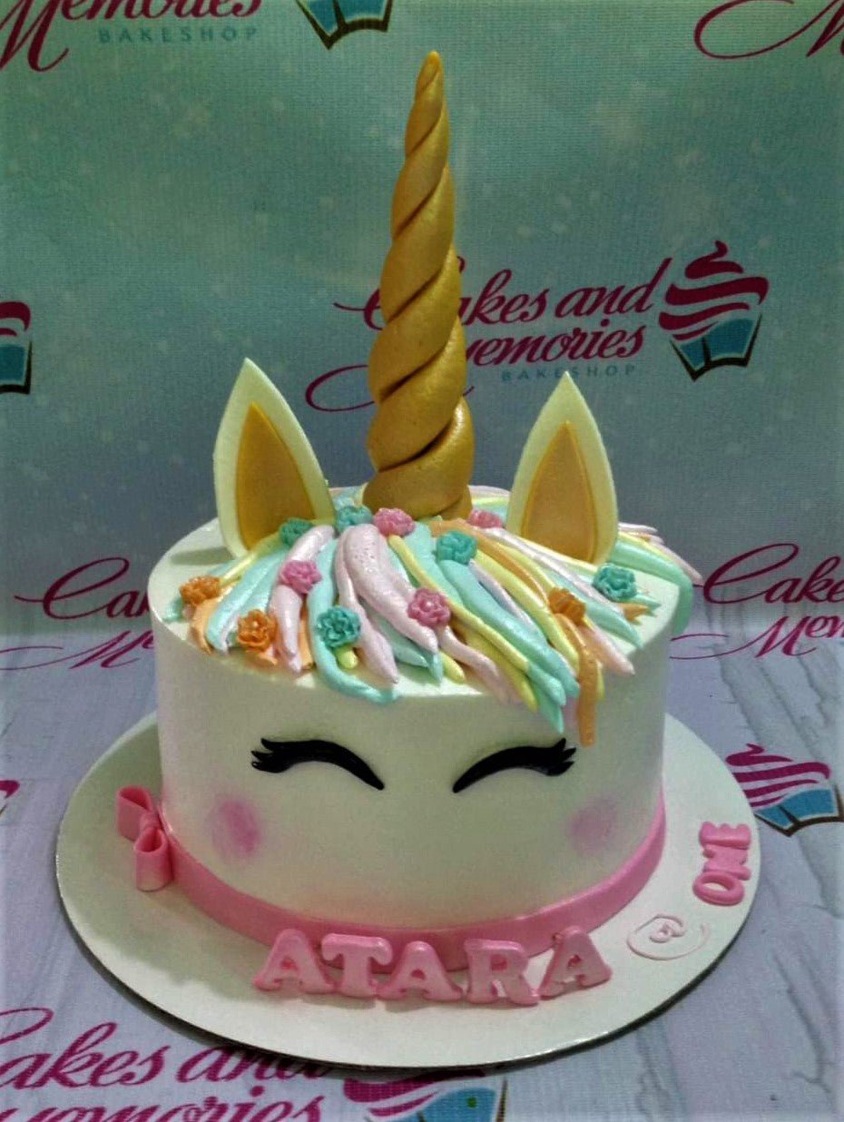 White unicorn cake with a gold horn, ears, and colorful pastel icing mane with small flowers and a pink base ribbon. White unicorn cake with a gold horn, ears, and colorful pastel icing mane with small flowers and a pink base ribbon.