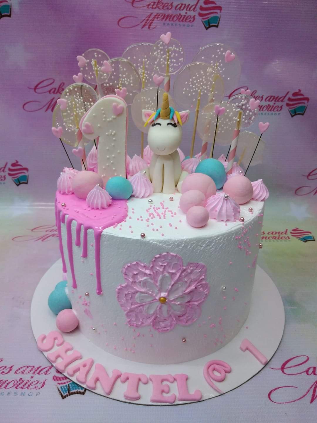 White 1-tier unicorn birthday cake with pink drip, isomalt lollipops, and a fondant unicorn figure. White 1-tier unicorn birthday cake with pink drip, isomalt lollipops, and a fondant unicorn figure.