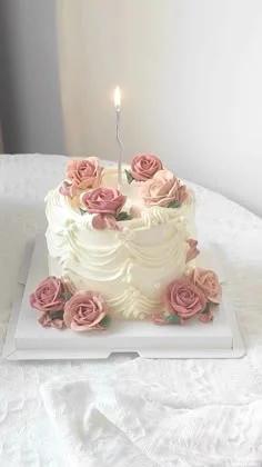 Elegant white vintage-style cake with pink and peach icing roses and a single silver candle.