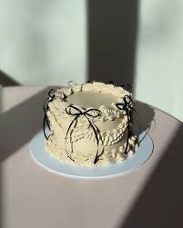 Vintage-style white minimalist cake with intricate cream piping and black ribbon bows.
