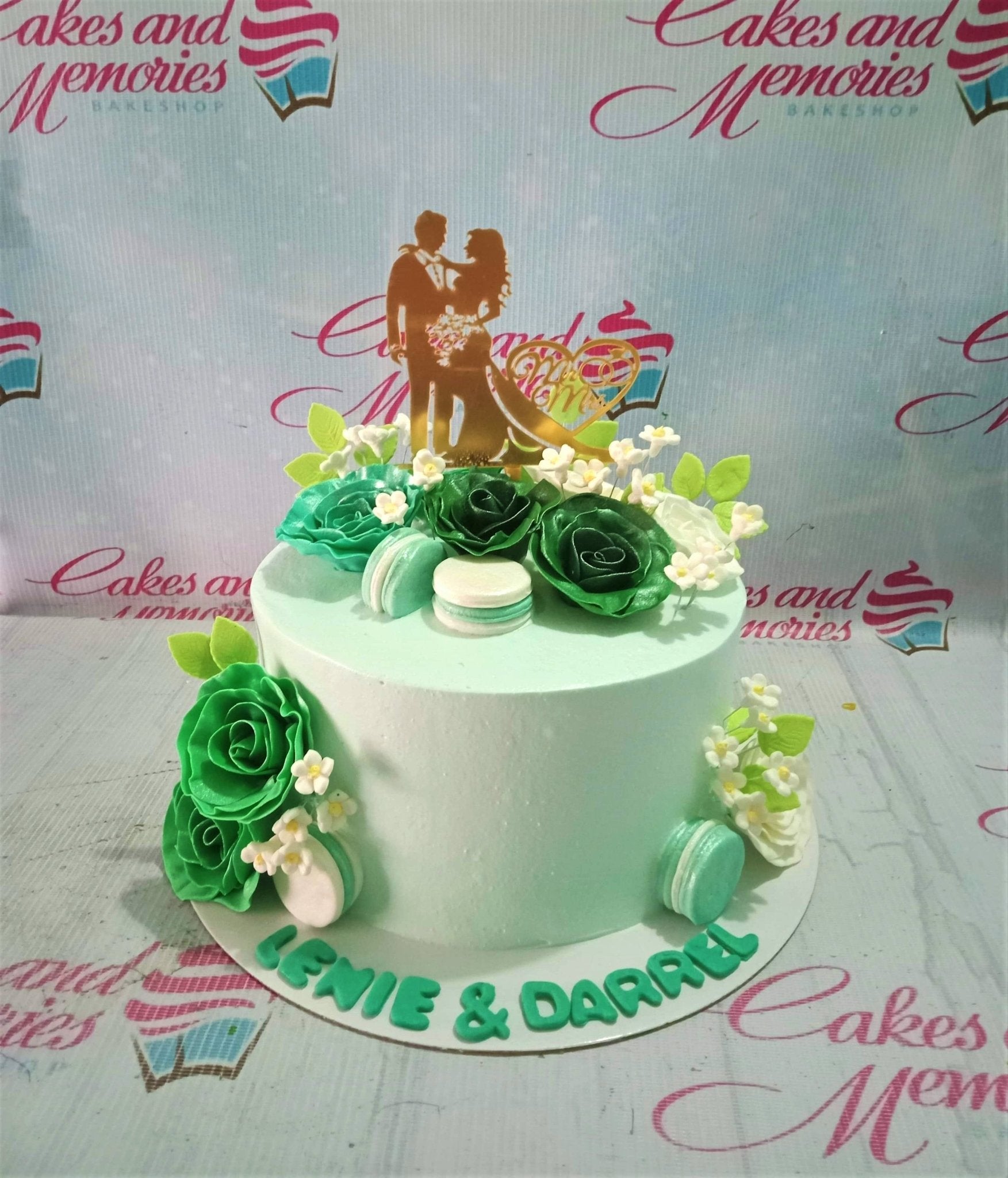 Mint green wedding cake with dark green and white gumpaste roses, macarons, and a gold bride and groom topper. Mint green wedding cake with dark green and white gumpaste roses, macarons, and a gold bride and groom topper.
