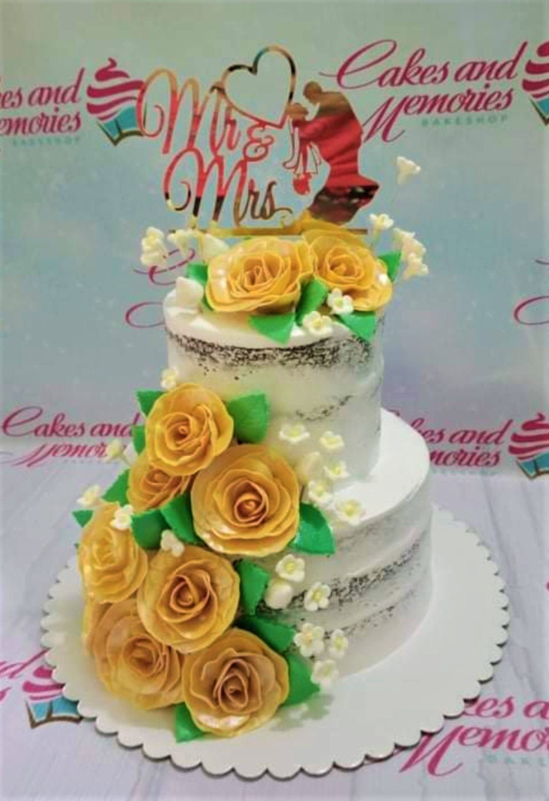 Two-tier semi-naked chocolate cake decorated with large yellow gumpaste roses and a gold Mr & Mrs topper. Two-tier semi-naked chocolate cake decorated with large yellow gumpaste roses and a gold Mr & Mrs topper.