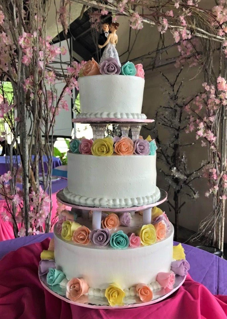 Elegant three-tier white wedding cake with colorful gumpaste roses and a bride and groom topper on a tiered stand. Elegant three-tier white wedding cake with colorful gumpaste roses and a bride and groom topper on a tiered stand.