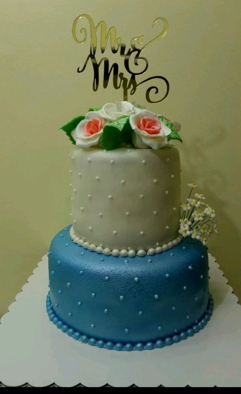 Two-tier wedding cake with a white top tier and blue bottom tier, decorated with white pearls, fondant roses, and a gold Mr & Mrs topper. Two-tier wedding cake with a white top tier and blue bottom tier, decorated with white pearls, fondant roses, and a gold Mr & Mrs topper.