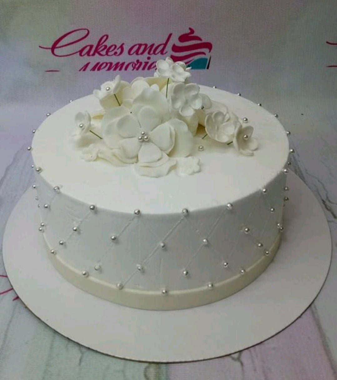 Elegant white single tier cake with white gumpaste flowers and silver dragees in a quilted pattern. Elegant white single tier cake with white gumpaste flowers and silver dragees in a quilted pattern.