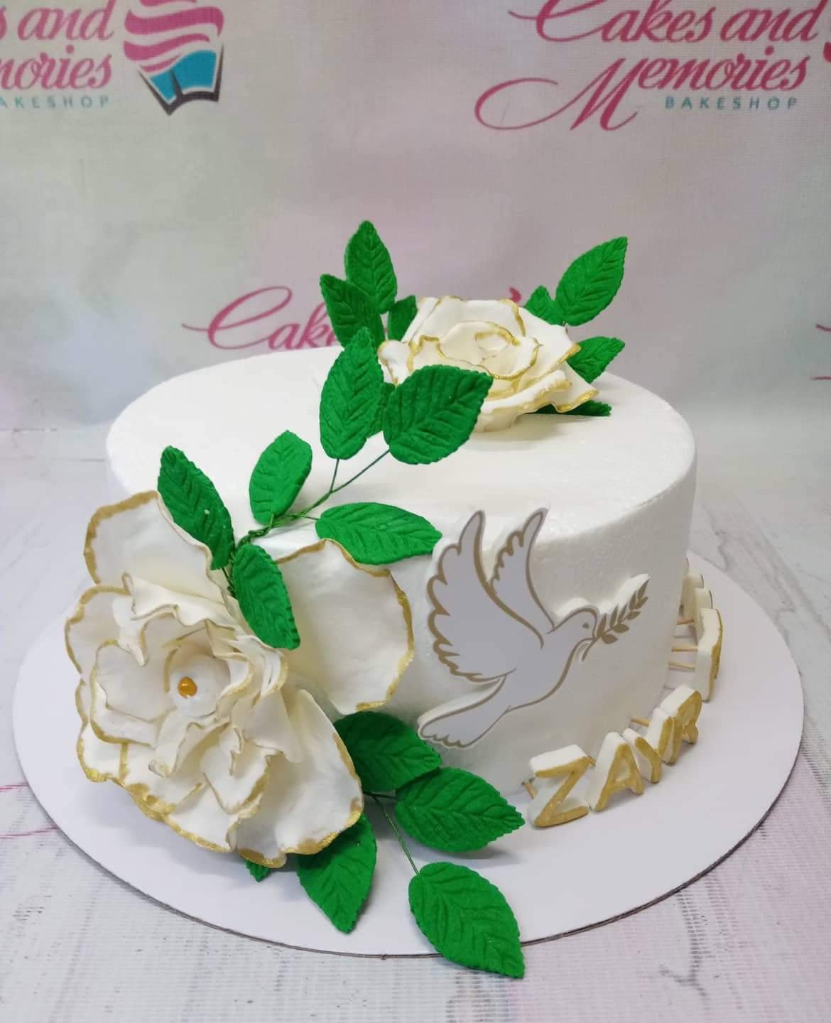 White 1-tier baptismal cake with large white gumpaste roses, green leaves, a white dove printout, and gold gumpaste letters. White 1-tier baptismal cake with large white gumpaste roses, green leaves, a white dove printout, and gold gumpaste letters.