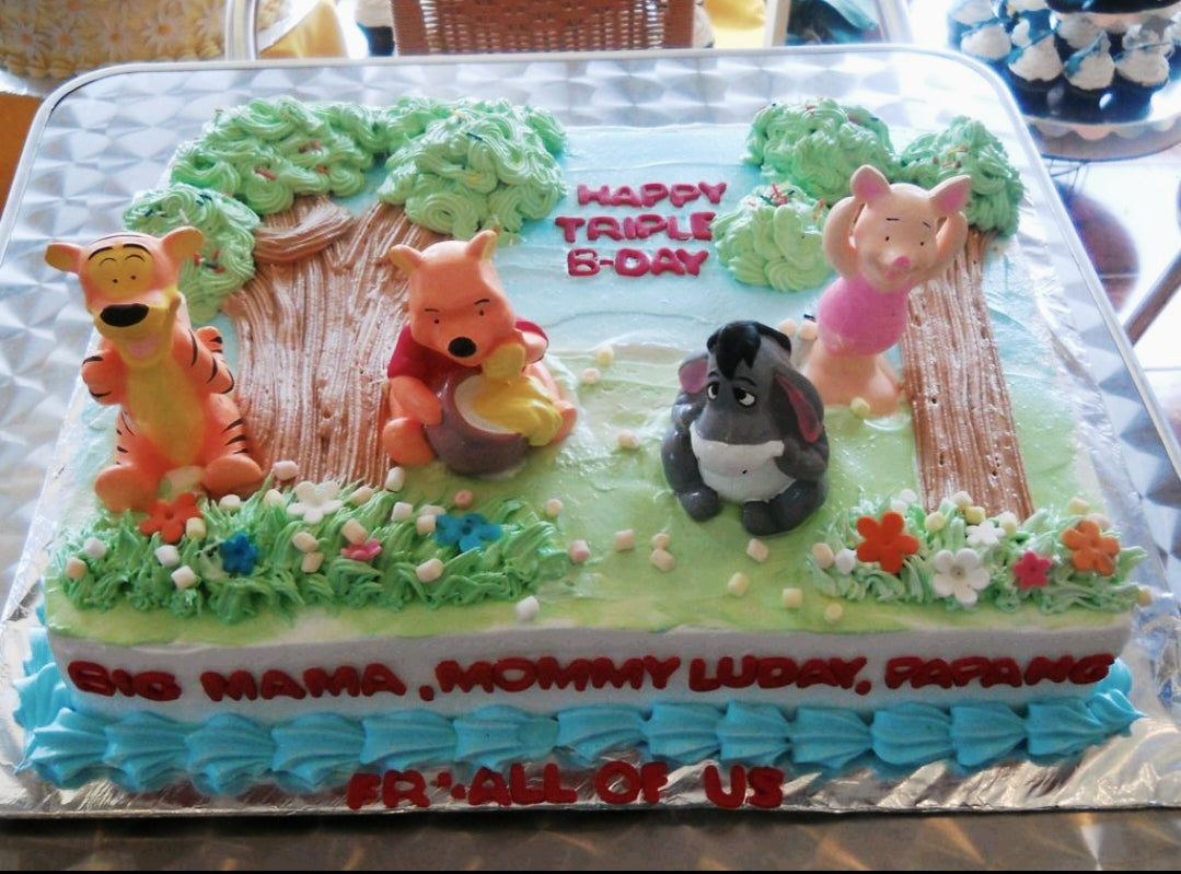 Winnie the Pooh themed rectangle cake with 3D figures of Pooh, Tigger, Eeyore, and Piglet in a forest setting with green icing trees. Winnie the Pooh themed rectangle cake with 3D figures of Pooh, Tigger, Eeyore, and Piglet in a forest setting with green icing trees.