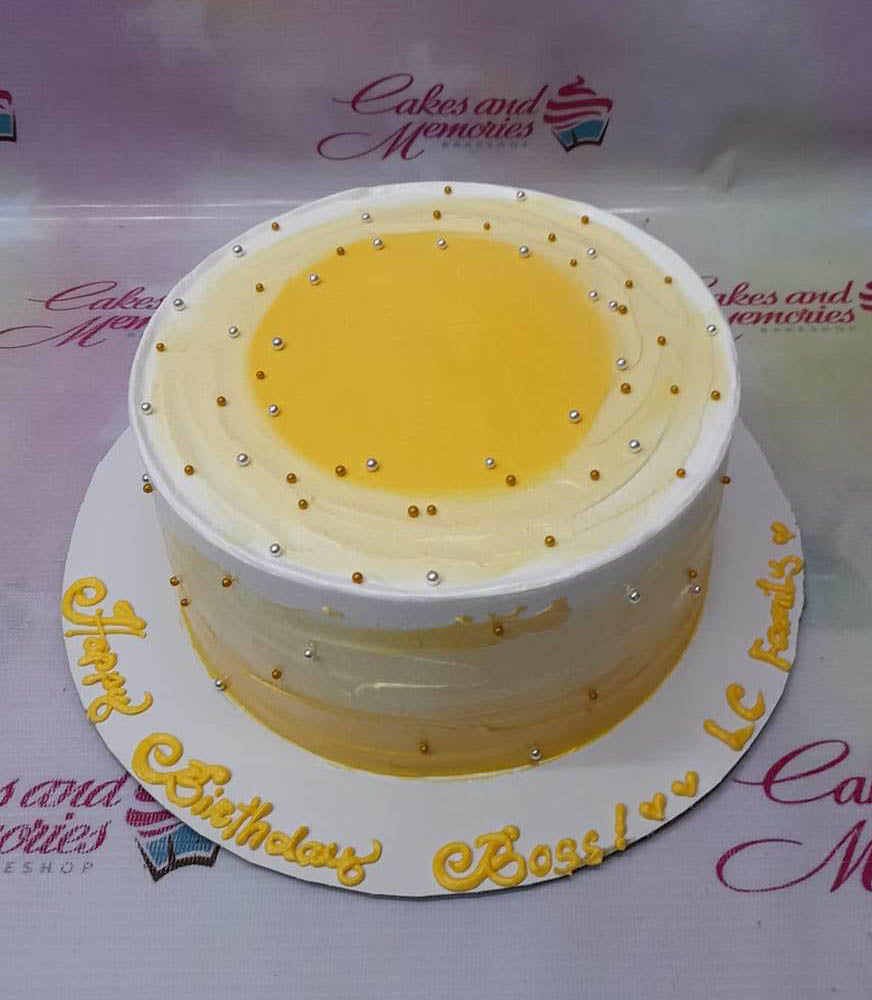 Round yellow and white minimalist cake with gold and silver dragees and a yellow icing message on the base board. Round yellow and white minimalist cake with gold and silver dragees and a yellow icing message on the base board.