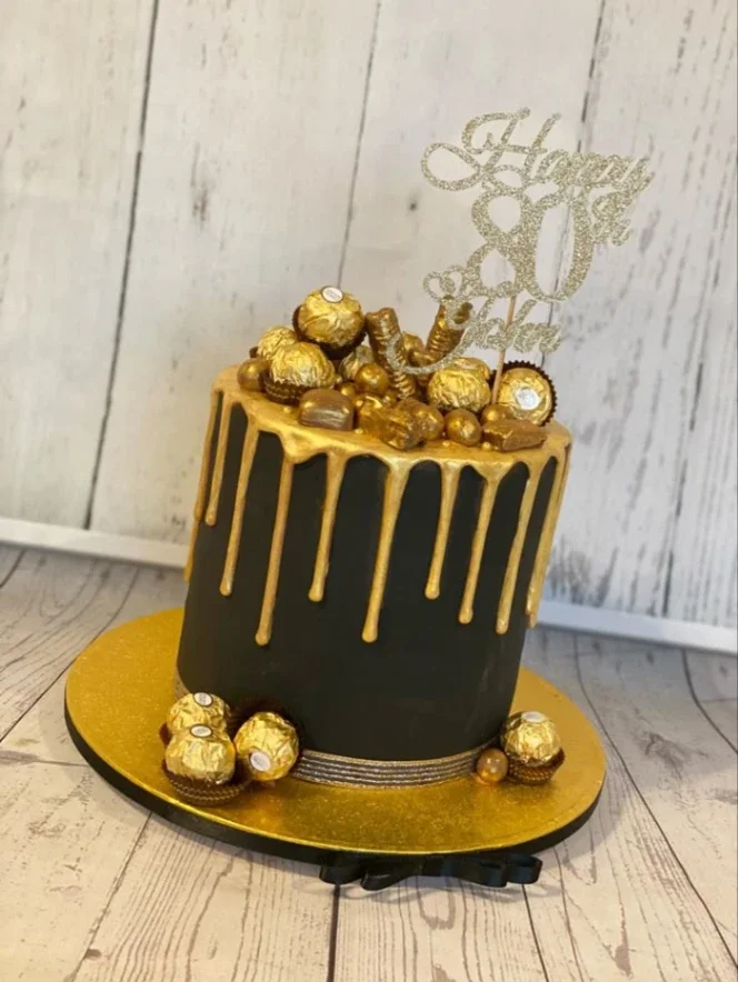 Tall black cake with gold drip, topped with Ferrero Rocher chocolates and a gold glitter Happy 80th John topper.