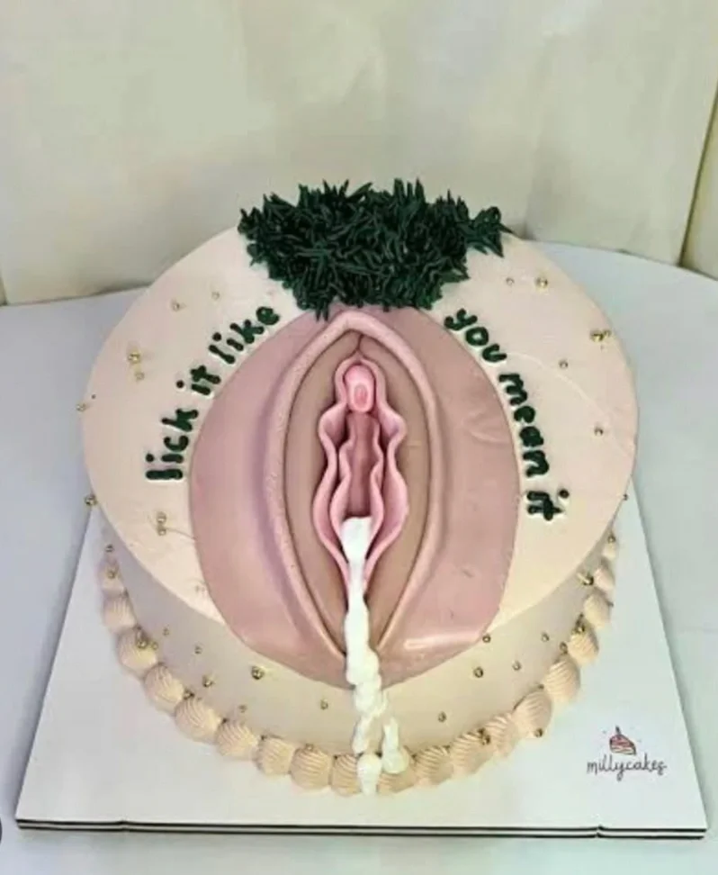 A round beige cake featuring a detailed 3D edible gumpaste vulva design with dark green icing hair and white icing drip. A round beige cake featuring a detailed 3D edible gumpaste vulva design with dark green icing hair and white icing drip.