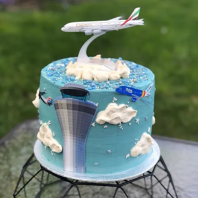 Light blue 1-tier birthday cake with soft icing, an airplane toy, printed control tower, and piped clouds Light blue 1-tier birthday cake with soft icing, an airplane toy, printed control tower, and piped clouds