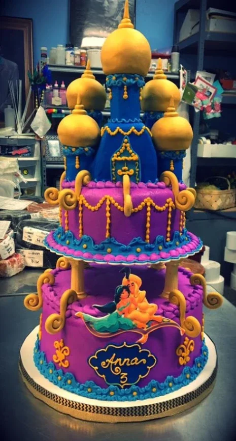 Two-tier purple and blue Aladdin themed castle cake with Jasmine and Aladdin printout and gold dome toppers. Two-tier purple and blue Aladdin themed castle cake with Jasmine and Aladdin printout and gold dome toppers.