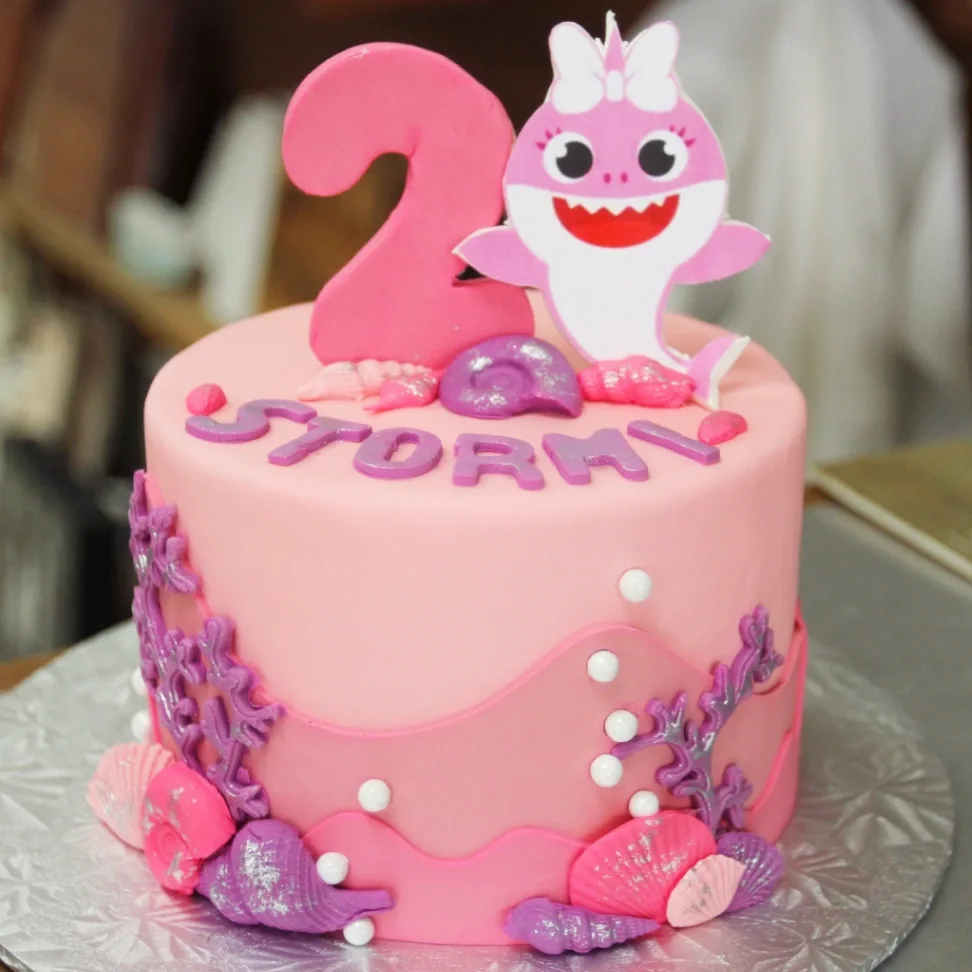 Pink Baby Shark themed fondant cake with edible sea shells, coral, and a pink shark printout for a 2nd birthday. Pink Baby Shark themed fondant cake with edible sea shells, coral, and a pink shark printout for a 2nd birthday.
