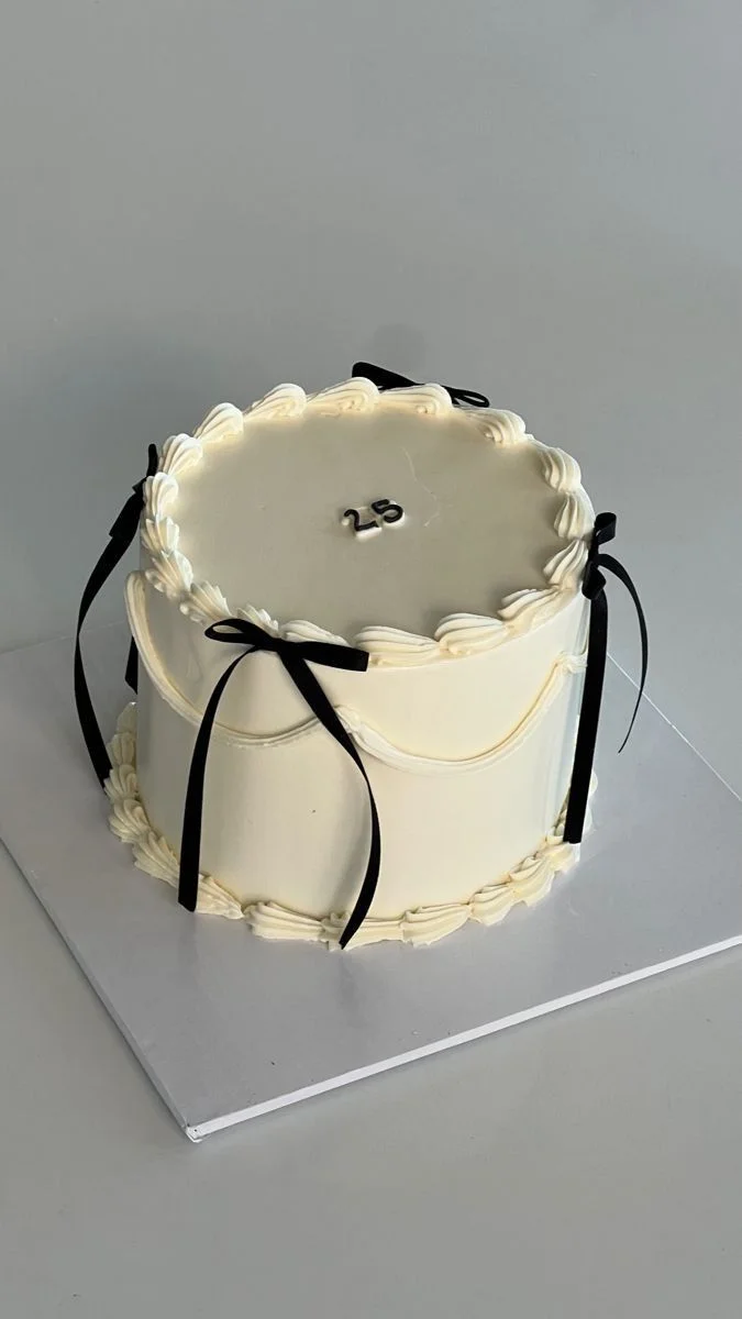 Elegant white minimalist cake with black satin ribbons and a small 25 topper on top. Elegant white minimalist cake with black satin ribbons and a small 25 topper on top.