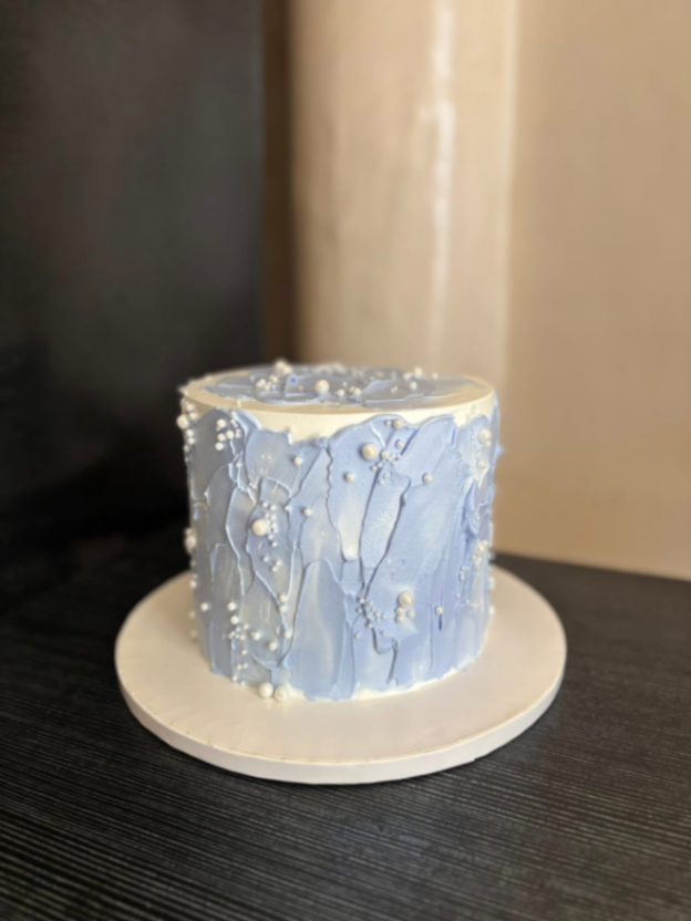 A single tier white cake with textured light blue palette knife icing and white pearl sprinkles on a white baseboard. A single tier white cake with textured light blue palette knife icing and white pearl sprinkles on a white baseboard.