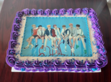 Rectangle BTS K-pop themed cake with a large group photo printout, purple piped icing borders, and blue sprinkles. Rectangle BTS K-pop themed cake with a large group photo printout, purple piped icing borders, and blue sprinkles.
